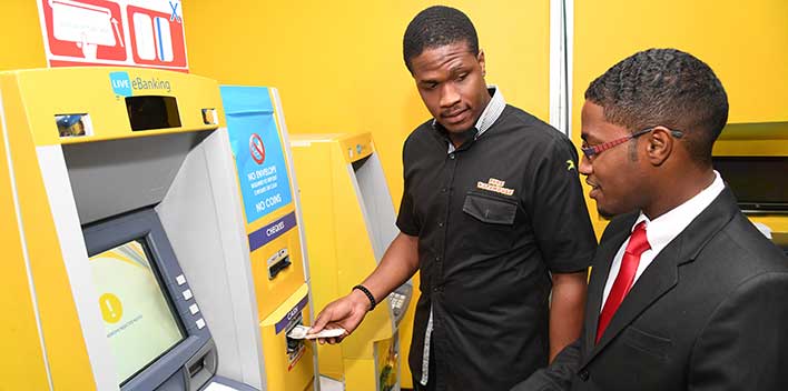 Ricardo Dystant, head of eBusiness at the JN Bank (left), assists Chavon Barnes, JN member, in using the card-less ATM machine at the JN Bank’s Half-Way-Tree branch in St Andrew.